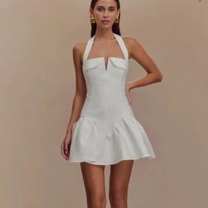 Vit kort klänning med volangkjol - Supersnygg vit kort klänning. Köpte till min student, men den kom aldrig. Helt oöppnad, och ny. Perfekt klänning till semester, fest, och sommartider. Nypris: 1250 kr.