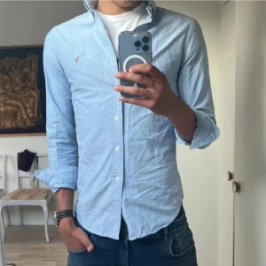 Ljusblå skjorta från Ralph Lauren - Klassisk ljusblå skjorta från Ralph Lauren med broderad logga på bröstet. Slim fit-modell med långa ärmar och knappar framtill. Skjortan är i bomull och har en stilren, tidlös look som passar perfekt till jeans eller chinos. Storlek S passar även Xs bäst pris på marknaden så var snabba !!