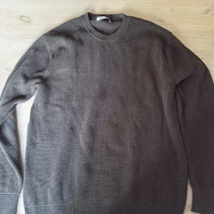 Grå stickad tröja från Zara - En stilren grå stickad tröja från Zara i klassisk modell med rund halsringning. Tröjan har ribbade muddar vid ärmslut och nederkant, och är perfekt för lager-på-lager. Passar dig som gillar en enkel men snygg look.