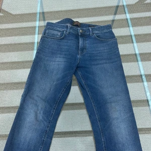 Blå jeans från Next Denim Goods Co - Snygga blå jeans från Next Denim Goods Co/ NEXT med klassisk femficksdesign och läderpatch bak. Jeansen har en rak passform och är tillverkade i slitstarkt denimtyg. Perfekta för en avslappnad och stilren look. Helt oanvända superbra skick!