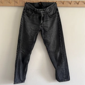 Mörkgrå Lee jeans W32 L32 - Mörkgråa jeans från Lee i modellen Oscar. Jeansen har klassisk femficksdesign, raka ben och normal passform. Tillverkade i slitstarkt denimtyg med en mörk tvätt, perfekt till sneakers eller boots.