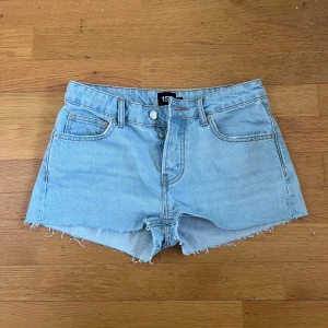 Ljusblå jeansshorts  - Ljusblå jeansshorts från 157 med råa kanter och klassisk femficksdesign. Shortsen är lowrise och stängs med knappar framtill. 