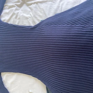 Mörkblå ribbad stickad klänning GANT - Supersnygg mörkblå stickad klänning från GANT i ribbat material. Klänningen har en tight passform och är perfekt för dig som gillar en stilren look. Den är ärmlös och har en klassisk rund halsringning. Perfekt att styla med sneakers eller boots.