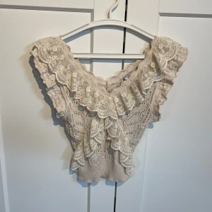 Beige stickad topp med spetsvolang - Supersöt beige stickad topp med breda spetsvolanger längs axlar och halsringning. Toppen är ärmlös och har ett vackert virkat mönster. Köpt på Zara för ett bra tag sedan men endast använd vid några enstaka tillfällen. Mycket bra skick och i storlek S.💕