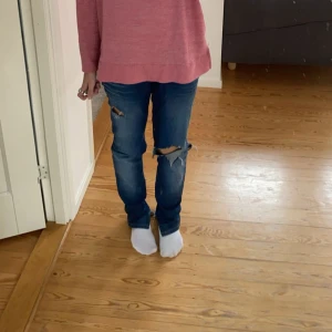 Blå slitna jeans med hål - Säljer ett par blå jeans med slitningar och stora hål på båda benen. Jeansen har en rak passform och klassisk femficksdesign. Perfekta för en avslappnad och trendig look.