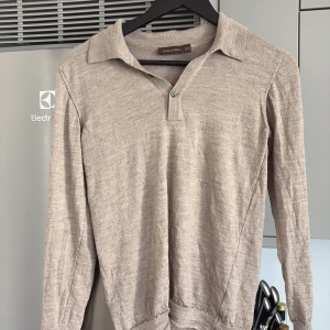 Beige pikétröja från Oscar Jacobson - Snygg beige pikétröja från Oscar Jacobson med klassisk krage och knappslå. Tröjan är långärmad och har en mjuk, stickad känsla i bomullsmix. Perfekt för dig som gillar en clean och stilren look.