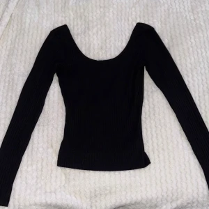 Svart ribbad långärmad topp NA-KD - En svart ribbad långärmad topp från NA-KD med djup rundad urringning. Snygg och enkel modell som sitter tight. Storlek XXS men sitter som xs/s