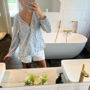 Blommig blus  - Supersöt blus med blått och vitt blommönster, v-ringning och snörning vid halsen. 