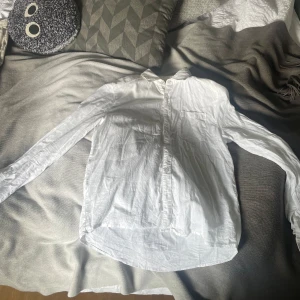 Linne skjorta  - Klassisk vit skjorta i linne med  bröstficka. Skjortan har knappar framtill och en rak passform som funkar till många olika stilar. Perfekt att bära öppen över en t-shirt eller knäppt för en clean look. Passar både tjejer och killar skulle jag säga. Storlek 158-164 köpt på kids brandstore för ca 700 kr