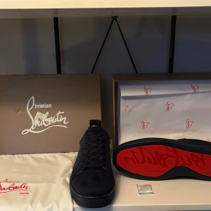Christian Louboutin Louis N Luck Velour - Snygga svarta sneakers från Christian Louboutin i mjuk mocka med ikonisk röd sula. Skorna har rund tå, svarta snören och diskret broderad logga på hälen. Insidan är ljusbeige och sulan är platt. Perfekt för dig som vill sticka ut med exklusiv stil.