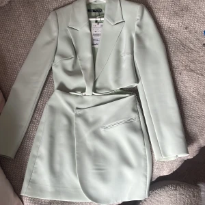 Ljusgrön kavaj och kjol från Zara - Snygg ljusgrön kostym från Zara med croppad kavaj och matchande kjol. Kavajen har klassisk krage och långa ärmar, kjolen har en stilren fickdetalj. Kjolen samt kavajen sitter ihop.