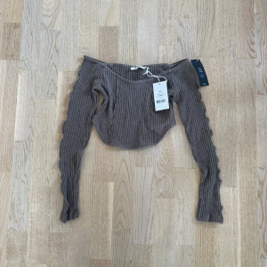 Ribbad offshoulder topp från NA-KD - Säljer en ribbad grå offshoulder topp från NA-KD i croppad modell. Toppen har långa ärmar med vågiga detaljer längs sidorna och är tillverkad i mjuk bomullsmix. Perfekt för dig som gillar trendiga och bekväma plagg med snygg passform.