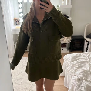 Olivgrön stickad klänning från Zara - Supersnygg olivgrön stickat sett från Zara med ribbade muddar, stora fickor framtill och halv dragkedja vid halsen. Jättefint inför hösten eller en kallare sommarkväll!