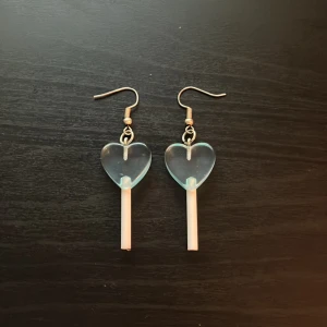 Blå hjärtformade örhängen - Säljer ett par unika örhängen med transparenta blå hjärtan och vita stavar som hänger ner. Perfekt för dig som vill sticka ut med ett lekfullt och trendigt smycke. Krokar i metall och cool design som drar blickarna till sig. Köp från kawaii shop i göreborg för några år sedan men aldrig använt.