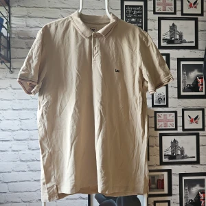 pikétröja från Lee - Snygg beige pikétröja från Lee i regular fit. Klassisk krage med knappar och diskret Lee-logga på bröstet. Tillverkad i mjuk bomull, perfekt för en clean och avslappnad stil. Passar dig som gillar enkel men stilren look.