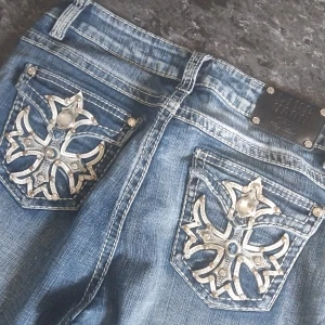  jeans med broderade bakfickor - Snygga blå jeans från Live Hard med unika broderade detaljer och pärlor på bakfickorna. Klassisk femficksmodell med raka ben och kontrastsömmar. Jeansen har normal passform och cool slitning för en avslappnad look.
