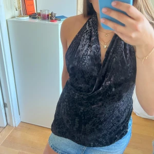 Svart halterneck topp i sammet - Säljer en svart halterneck topp i sammet med subtilt leopardmönster. Toppen är urringad och har öppen rygg.