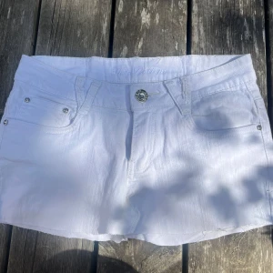 Vita jeansshorts Hot Bottom med dragkedjor - Snygg vit jeanskjol från Hot Bottom med rå kant nertill, klassisk femficksmodell och coola dragkedjor på bakfickorna. Silverfärgade detaljer och knapp framtill. Perfekta för varma dagar när du vill ha en fräsch och clean look.