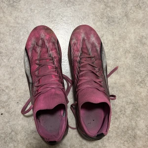 Puma Ultra rosa fotbollsskor - Säljer ett par Puma Ultra fotbollsskor i en snygg rosa färg med svarta och vita detaljer. Skorna har snörning, låg profil och mönstrad ovandel i syntetmaterial. Perfekta för dig som vill sticka ut på planen med stil.