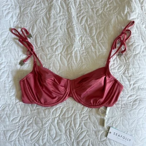 Rosa bikiniöverdel från Seafolly - Supersnygg rosa bikiniöverdel från Seafolly med bygel och justerbara axelband med knyt och detaljer med fjärilar. Snygg metallspänne bak och glansigt material som ger en lyxig känsla. Perfekt för strandhäng och poolparty! Nypris 790 sek. 