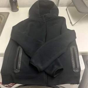 Svart Nike hoodiejacka XL  - Svart hoodiejacka från Nike i storlek XL. Jackan har hel dragkedja framtill, två fickor med dragkedja och en stor luva. Tillverkad i mjukt material som känns skönt mot huden. Perfekt för chill eller när du är på språng. Den är använd och har en liten del av fläkar som inte syns, går att ta bort de genom tvätt. Priser kan diskutera.