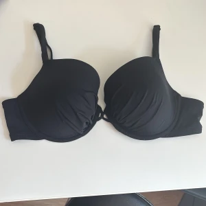 Bikinitopp - Svart bikinitopp från Lindex med bygel och lätt vadderade kupor. Knytdetalj mellan kuporna och smidig knäppning bak. Köparen står för eventuell fraktkostnad:)