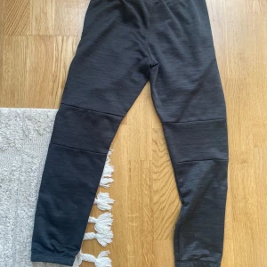 Svarta mjukisbyxor från SOC - Svarta mjukisbyxor från SOC med elastisk midja och tekniskt material som andas. Byxorna har smal passform och är perfekta för träning eller chill. Snygg sportig look med diskret logga i midjan och bekvämt tyg som håller dig torr.