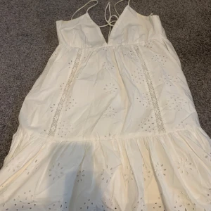 Vit sommarklänning från Zara - Superfin vit klänning från Zara med tunna axelband och v-ringning. Klänningen har broderade blommor och spetsdetaljer, samt en luftig och flowy passform. Perfekt för varma dagar och ger en fräsch och romantisk vibe.