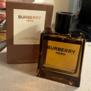 Burberry Hero Eau de Parfum 100ml - Burberry Hero Eau de Parfum i en stilren, fyrkantig glasflaska med bärnstensfärgad ton och svart kork. Kommer i original brun kartong med vit etikett. Flaskan rymmer 100 ml. parfym har testats bara en gång, köparen står för frakten, priset kan diskuteras.