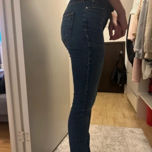 Mörkblå jeans från Gina Tricot - Säljer ett par mörkblå skinny jeans från Gina Tricot, modell Perfect Jeans. De är högmidjade, stretchiga och har ett litet hål på varsin ficka, synd knappt (se sista bilden)