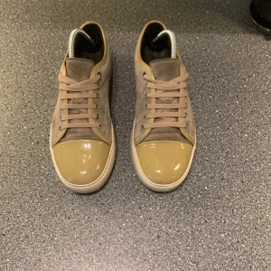 Beige lanvins skor - Snygga beigea sneakers från Lanvin med olivgröna detaljer och snörning. Skorna har en rund tå och är tillverkade i mocka med en stilren design. Perfekta för en trendig look. En liten skada inuti skon som du ser på sista bilden och sulan är bytt till en ny svart. Storlek uk 7 sitter 42-43