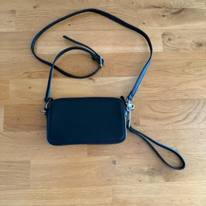Svart axelväska i skinn från Zara - En stilren svart axelväska i skinn från Zara. Enkel design som passar till det mesta. Perfekt storlek för mobil, plånbok och nycklar. Använt 1 gång!