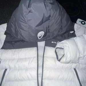 Grå dunjacka från Sail Racing M - Säljer en grå dunjacka från Sail Racing i storlek medium. Jackan har en stor huva med logga, dragkedja framtill och quiltad design. Perfekt för kalla dagar och har en clean look med diskreta ränder i tyget. Pris Kan gå ner I snabb köp