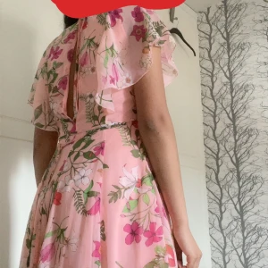 Rosa blommig långklänning Bik Bok XS - Superfin klänning från Bik Bok i ljusrosa med blommigt mönster. Klänningen har volangärmar, hög hals och en snygg öppen detalj i ryggen. Flowy material som känns lätt och somrigt. Perfekt för dig som vill sticka ut med en romantisk look.