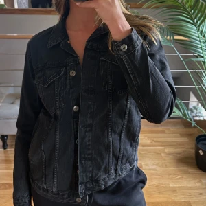 Svart jeansjacka med knappar - Säljer en svart jeansjacka med klassisk passform och snygga silvriga knappar framtill. Jackan har två bröstfickor och långa ärmar med knapp vid ärmslut. Perfekt till lager-på-lager och funkar året runt.
