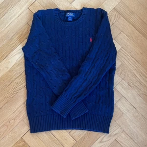 Stickad Polo Ralp Lauren tröja - En klassisk mörkblå stickad Polo Ralph Lauren tröja. Köpt för många år sedan men har inte använts på länge och är fortfarande i mycket bra skick; inga defekter. Tröjan är i barnstorlek och passar dig som är mellan 14-16 år eller 150-161cm lång.