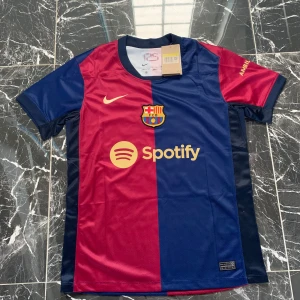 FC Barcelona Lamine Yamal matchtröja - Snygg FC Barcelona matchtröja med Lamine Yamal och nummer 19 på ryggen. Tröjan är kortärmad och har klassiska blå och röda fält, klubbmärke på bröstet och Spotify-logga. Tillverkad i lätt och ventilerande polyester, perfekt för fotboll eller att bära som supporter.