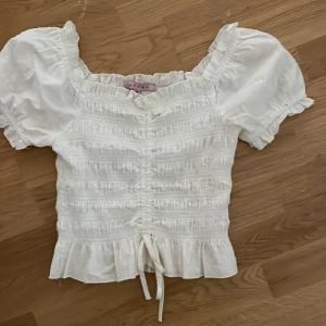 Vit blus med puffärm  - Supersöt vit blus med puffiga korta  Toppen har knytning framtill och rynkade detaljer. Perfekt sommar och vår 💗💗skriv gärna vid funderingar 