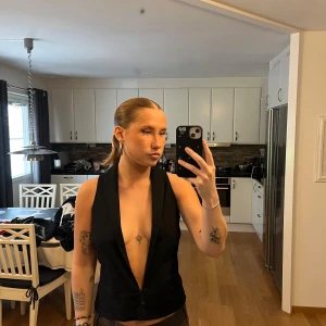 Svart omlott väst med djup v-ringning  - Säljer en svart väst med djup v-ringning och omlottkänsla framtill. Västen är ärmlös, har knäppning med tre knappar och en klassisk krage. Västen är från Vero Moda i storlek 38 (S)