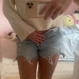 Ljusblå slitna jeansshorts med knappar, medelhög midja - Säljer ett par ljusblå jeansshorts med medelhög midja och flera slitningar och fransiga kanter. Shortsen har knappgylf och klassiska fickor både fram och bak.