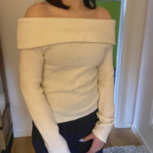 Offshoulder ribbad stickad tröja - Superfin offshoulder tröja i ljusbeige stickat material. Tröjan är ribbad och har långa ärmar, sitter tight och har en bred krage som vilar över axlarna. Perfekt för dig som vill ha en trendig och mysig look.
