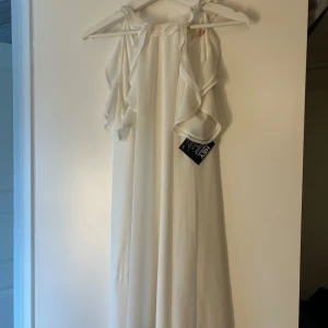 Vit långklänning från NLY Eve - Superfin vit långklänning från NLY Eve med volangdetaljer längs axlarna och halsringningen. Klänningen är ärmlös och har en luftig, flowy passform i tunt, lätt material som ger en romantisk känsla. Perfekt för speciella tillfällen när du vill sticka ut.❤️