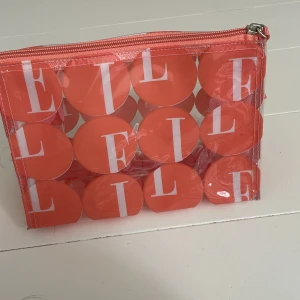 Transparent necessär från ELLE  - Transparent plast necessär från ELLE med orange cirklar och vita bokstäver. Väskan har dragkedja upptill och är perfekt för smink eller småprylar. Tillverkad i syntetmaterial. 