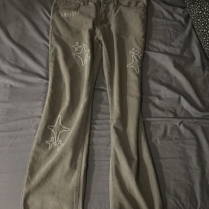 Grå jeans från Broken Planet Market - Unika grå jeans från Broken Planet Market med broderade vita stjärnor och texten 'BROKEN' framtill. Byxorna har raka ben, normal passform och klassisk femficksdesign. Materialet är robust bomull och jeansen har dragkedja och knapp i midjan.