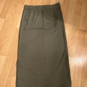 Olivgrön ribbad långkjol från Pieces - Snygg olivgrön långkjol från Pieces med ribbad struktur och slits på sidan. Kjolen har en elastisk midja och är i ett mjukt, stretchigt material som sitter skönt. Perfekt för dig som gillar en clean och chill stil.❤️