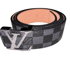 Louis Vuitton rutigt skärp med LV-spänne - Snyggt Louis Vuitton bälte i svart och grått med klassiskt rutigt Damier-mönster. Bältet har ett stort LV-spänne i silverfärgad metall och är gjort i exklusivt skinn. Perfekt accessoar för att lyfta din outfit med en lyxig touch.