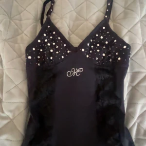 Svart linnetopp med pärlor och spets - Snygg svart linnetopp med pärldetaljer på bysten och axelbanden. Toppen har spets längs framsidan och ett glittrigt mönster i mitten. Köpte på second hand men aldrig använd. Kontakta mig för minsta lilla frågor💕