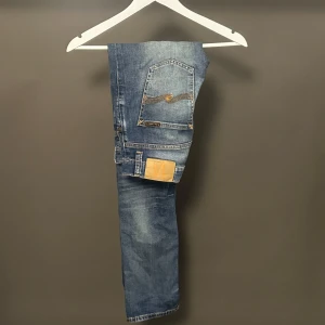 Nudie Jeans Grim Tim blå jeans 30/34 - Säljer ett par Nudie Jeans Grim Tim i tvätten Worn In Broken. Jeansen är blå med slitningar och har klassiska Nudie-detaljer på bakfickorna. Tillverkade i 98% ekologisk bomull och 2% elastan för lite stretch. Raka ben och normal passform.