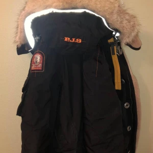 Svart Parajumpers dunjacka med päls - Säljer en svart Parajumpers dunjacka med snygga detaljer som gul rem vid kragen, patch på ärmen och stor huva med päls. Jackan har flera fickor, dragkedja och knappar framtill. Perfekt för kalla dagar och riktigt varm. STOR i storleken, jag är 183cm o den passar mer som en S