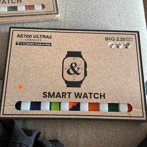 Smartwatch AE700 Ultra2 med flera armband - Säljer en AE700 Ultra2 smartwatch med stor 2.2-tums display. Klockan har fyrkantig silverfärgad boett och kommer med sju utbytbara silikonarmband i olika färger som svart, blå, grön, orange och mönstrat. Laddare och manual ingår. Perfekt för dig som gillar att byta stil ofta.